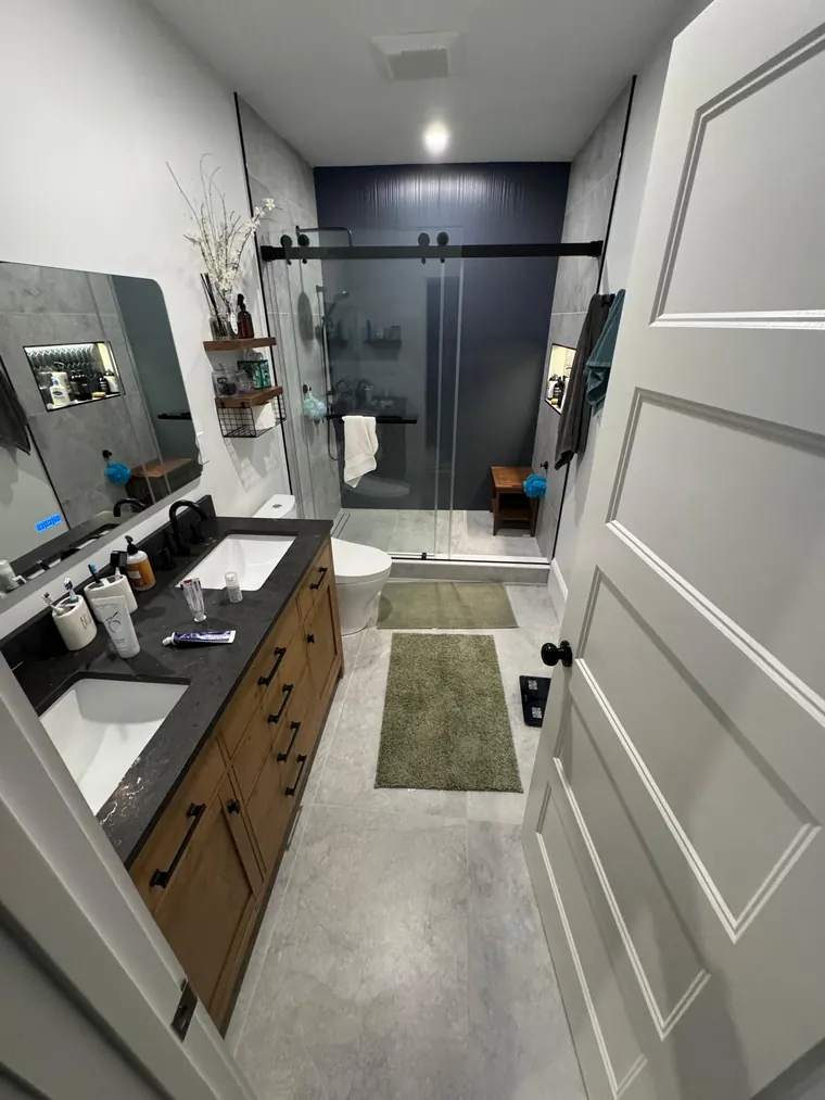 Glass shower enclosure beside a dark vanity in a remodeled bathroom