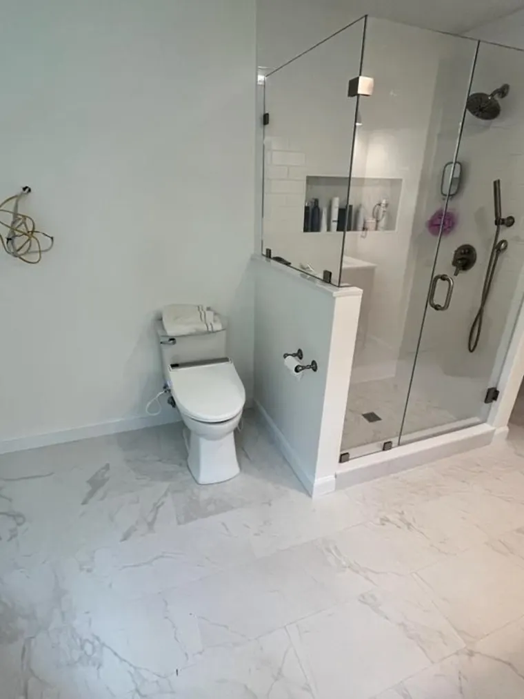 Bright bathroom with a corner glass shower and marble look floor tile